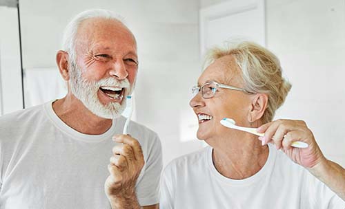 Two elderly parents brushing their teeth in their mobility bathroom, smiling