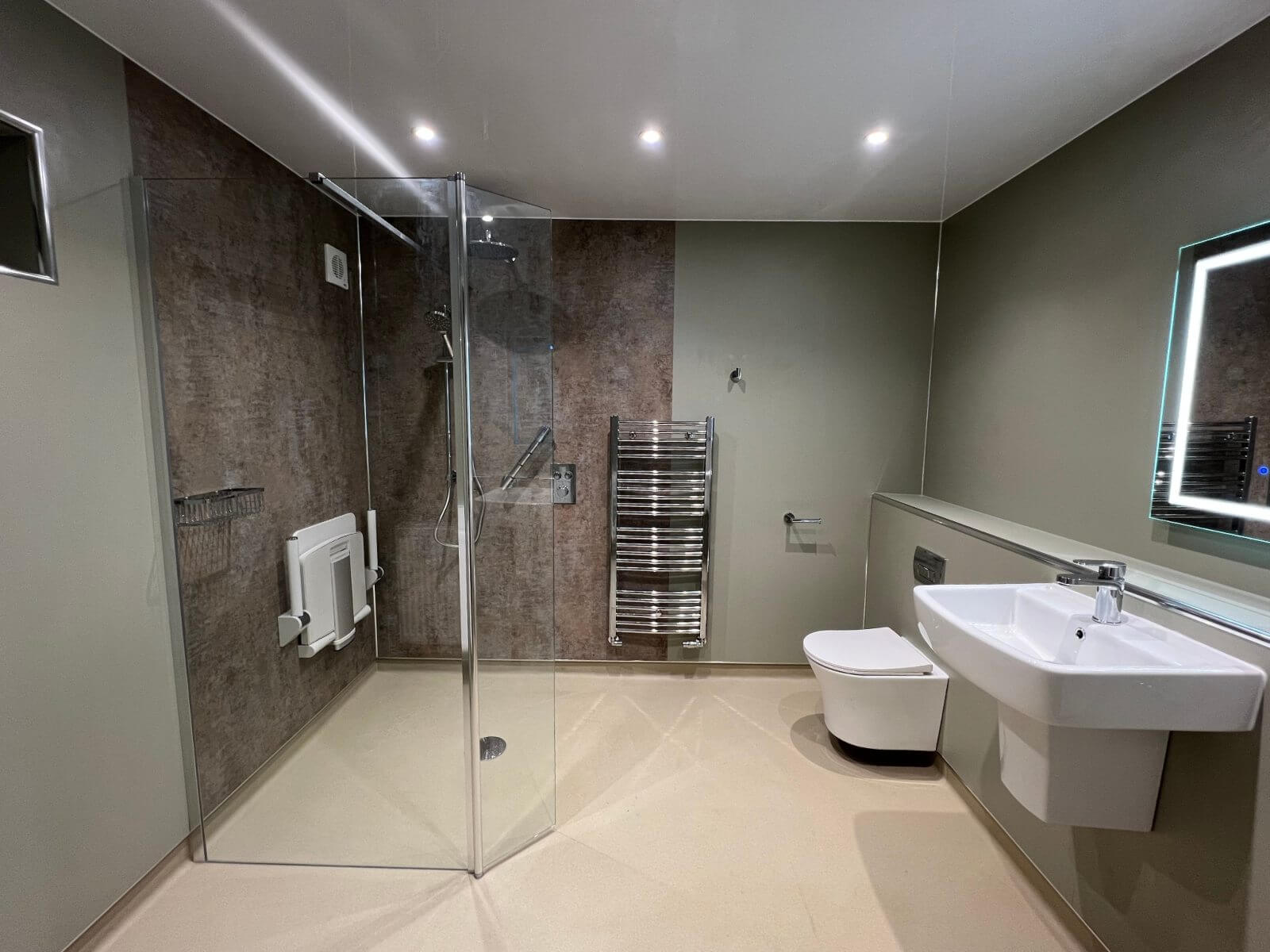 Spacious modern bathroom featuring walk‑in shower, wall‑mounted toilet, sink, and heated towel rail