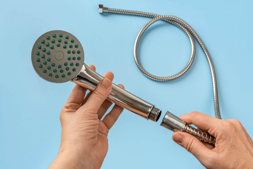 Hands attaching a flexible metal hose to a handheld shower head against blue background